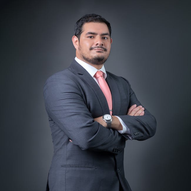 Professional portrait of a confident businessman in a gray suit with a pink tie, posing with arms crossed.